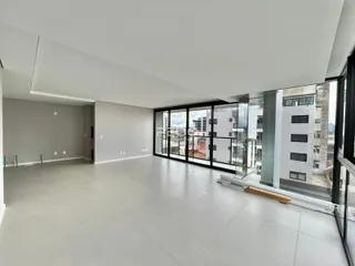 Ambiente interno de uma sala ampla com grandes janelas de vidro e vista para a cidade.