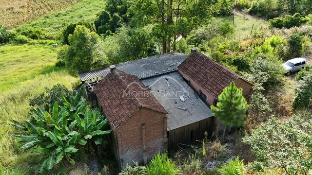 Fachada de uma construção rústica em meio a vegetação densa e colinas.