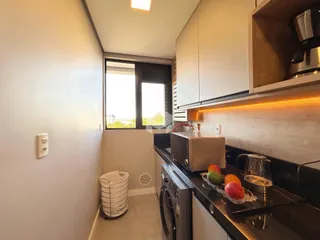 Vista da cozinha com armários brancos e bancada escura em um imóvel no Brasil.
