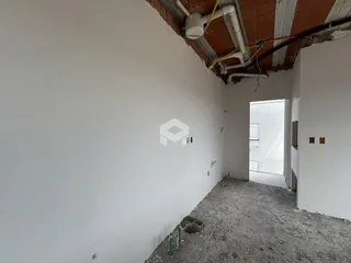 Vista interna de um ambiente com paredes brancas e teto exposto.