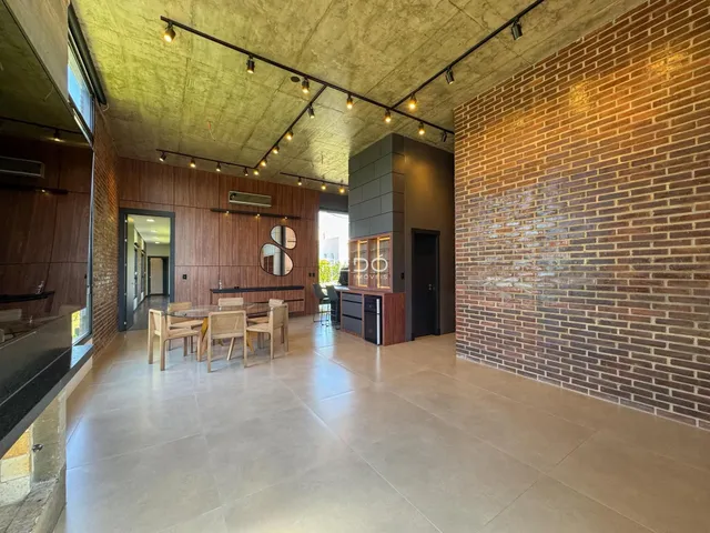 Ambiente interno de uma sala de estar e jantar com paredes de tijolo aparente e piso de porcelanato.