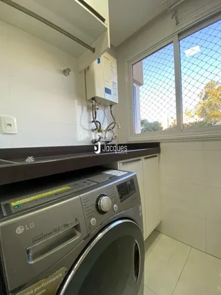 Foto de uma área de lavanderia com máquina de lavar e armários brancos.