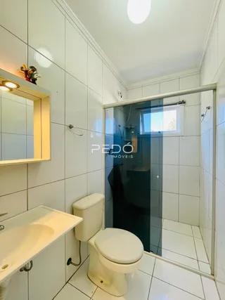 Banheiro com revestimento cerâmico branco e box de vidro transparente.