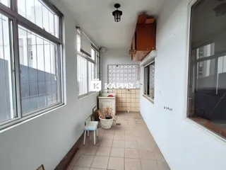 Uma foto interna mostra uma sala com grandes janelas e piso de cerâmica.
