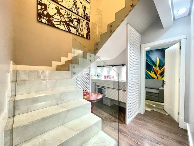 Vista de uma escadaria com degraus de mármore e guarda-corpo de vidro em uma residência.