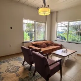 Foto interna de uma sala com grandes janelas e piso de madeira.