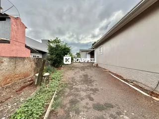 Vista externa de uma propriedade com um pátio de terra e vegetação ao lado de uma parede clara.