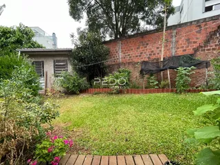 Vista externa de um quintal com gramado e muro de tijolos vermelhos.