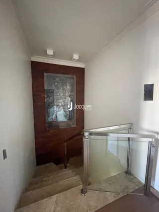 A foto mostra um corredor com escadaria e guarda-corpo de vidro.