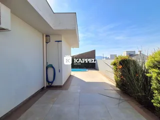 Vista de uma área externa com piso de porcelanato e piscina ao fundo.