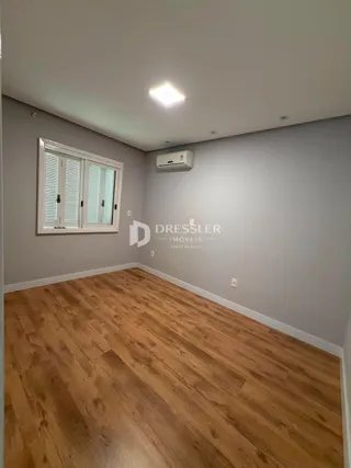 Vista interna de uma sala com piso de madeira clara e paredes cinzas.