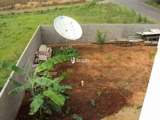 Vista de uma área externa com terra e vegetação ao lado de um muro de contenção.