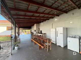 Vista interna de uma área coberta com mesa de madeira e geladeira em uma residência no Brasil.