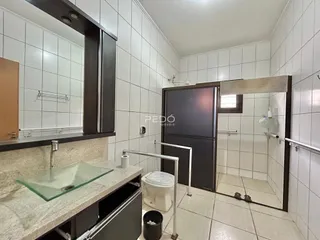 Interior de um banheiro com revestimento de azulejos brancos e box de vidro.