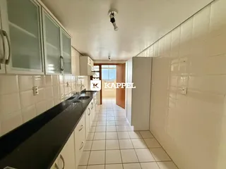 Vista de uma cozinha com armários brancos e piso de cerâmica em um corredor.