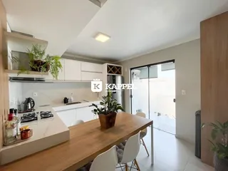 Vista de uma sala de jantar com mesa de madeira e cozinha moderna em um imóvel.