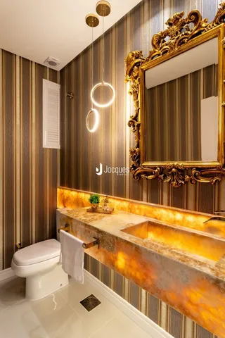 Foto de um banheiro com revestimento de parede em tons de dourado e espelho decorativo.