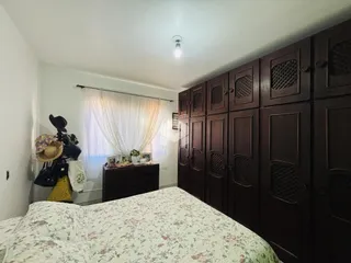 Quarto com armário de madeira escura e janela com cortinas brancas.