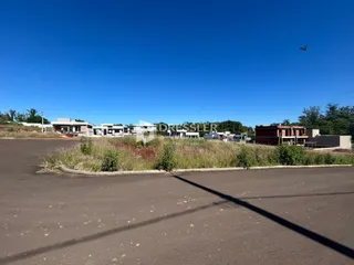 Vista externa de uma propriedade com construções ao fundo e vegetação na frente.