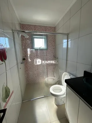 Banheiro com revestimento de azulejos brancos e box de vidro.