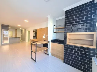 Ambiente interno de uma sala de estar ampla com piso claro e parede de tijolos escuros.