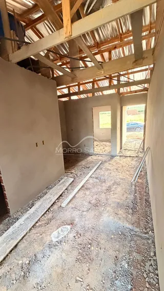 Interior de uma estrutura em construção com vigas de madeira expostas e piso de terra.