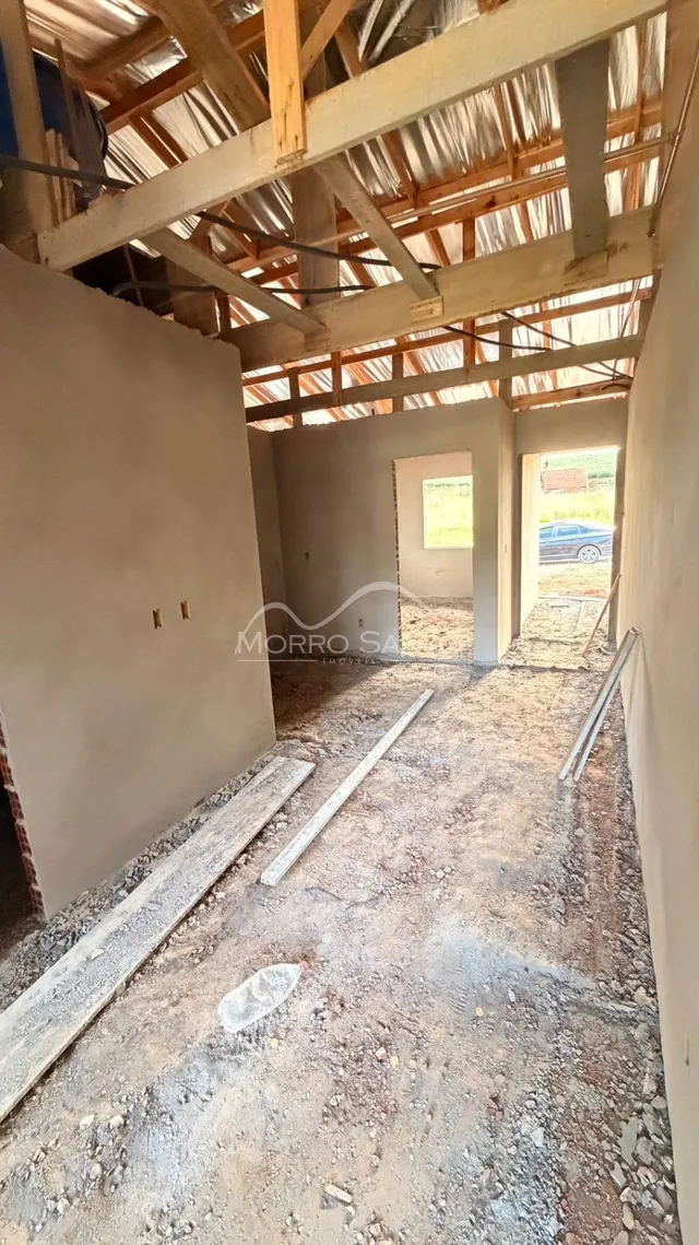 Interior de uma estrutura em construção com vigas de madeira expostas e piso de terra.