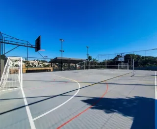 Imagem de uma quadra esportiva externa com marcações no chão sob um céu azul.