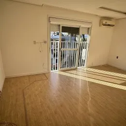 Foto interna de uma sala com piso de madeira clara e porta de vidro.