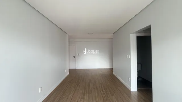 Corredor interno de uma residência com piso de madeira clara e paredes brancas.