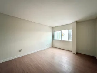 Ambiente interno de uma sala com piso de madeira clara e paredes brancas.