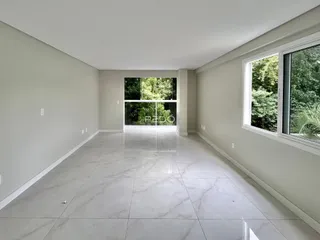 Ambiente interno amplo com piso de porcelanato claro e vista para a vegetação externa.