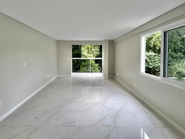 Ambiente interno amplo com piso de porcelanato claro e vista para a vegetação externa.