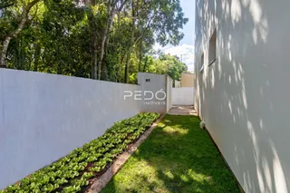 Vista externa de uma propriedade com muro branco e gramado lateral.