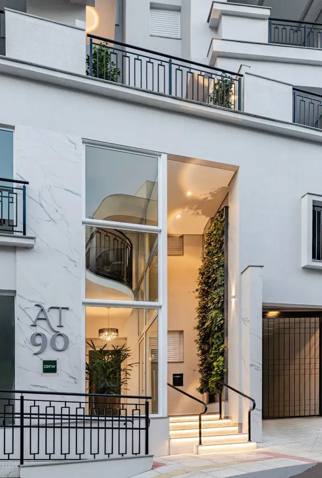 Fachada moderna de um edifício residencial com detalhes em vidro e vegetação.