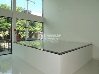 Vista interna de uma sala com grandes janelas e guarda-corpo de vidro.
