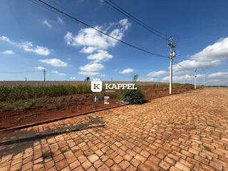 Vista externa de um pátio pavimentado com um campo aberto ao fundo sob um céu azul.