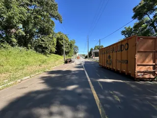 Vista de uma estrada com um contêiner de carga ao lado em uma área arborizada.