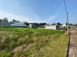 Vista externa de uma propriedade com grande área gramada e construções ao fundo.