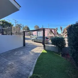 Vista externa do terreno com gramado e muro de contenção.