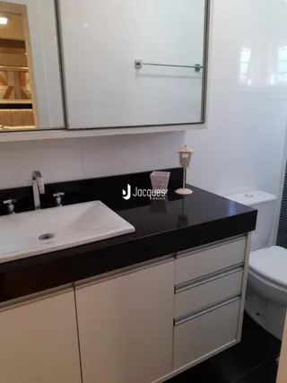 Vista de um banheiro com bancada escura e louças brancas.