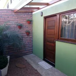 Fachada externa de uma residência com parede de tijolos aparentes e porta de madeira.