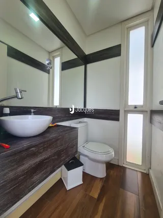 Banheiro moderno com bancada escura e piso de madeira.