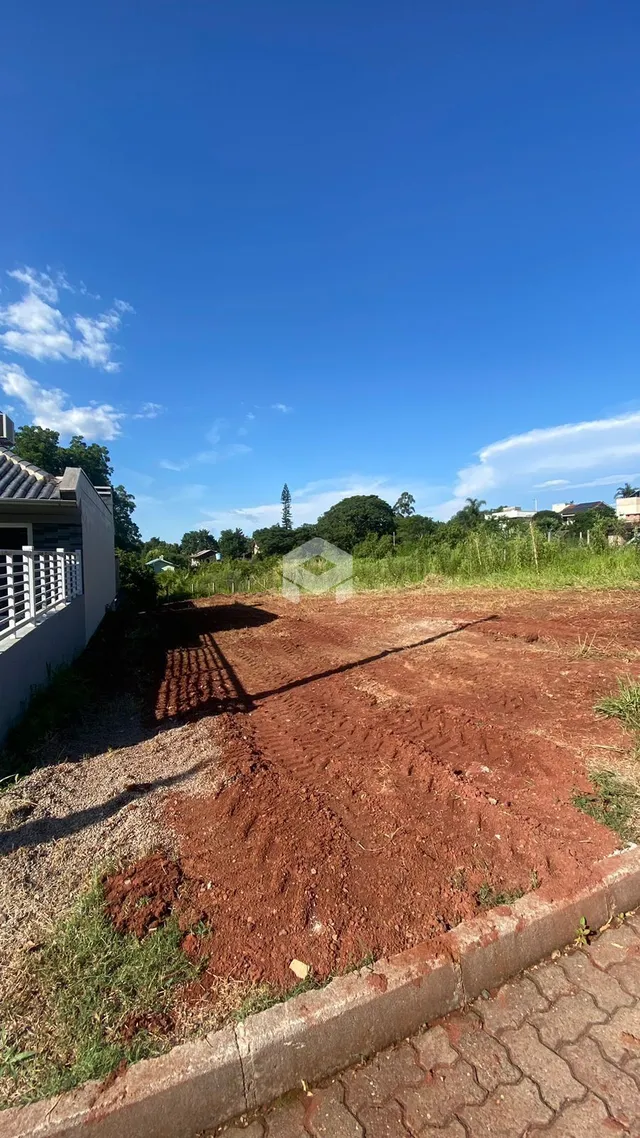 Vista externa de um terreno com solo de terra avermelhada e vegetação ao fundo.