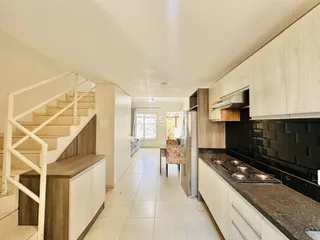 Vista de um corredor com escada e área de cozinha em um imóvel.
