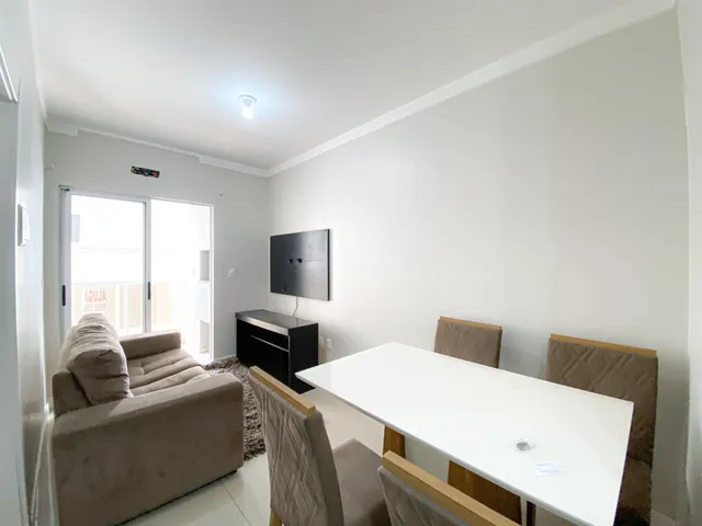 Sala de estar com sofá e mesa de jantar em um apartamento claro.