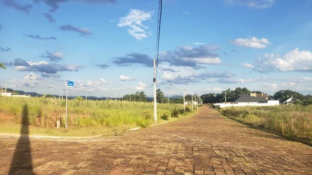 Vista externa de uma área pavimentada com vegetação seca sob um céu azul.