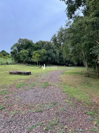 Paisagem externa de um terreno gramado com árvores ao fundo.