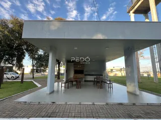 Vista externa de uma área coberta com pilares e piso de concreto.