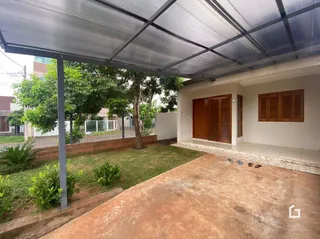 Vista externa de um quintal com piso de terra e grama sob uma estrutura de telhado metálico.